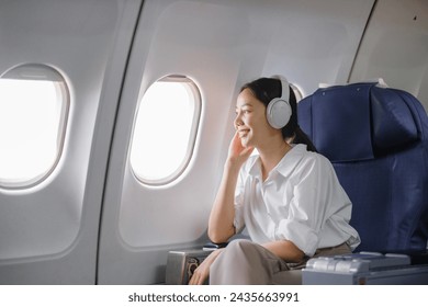 Asian woman sitting and using a smartphone in an airplane Listening to music next to the airplane seat window travel and technology concept - Powered by Shutterstock