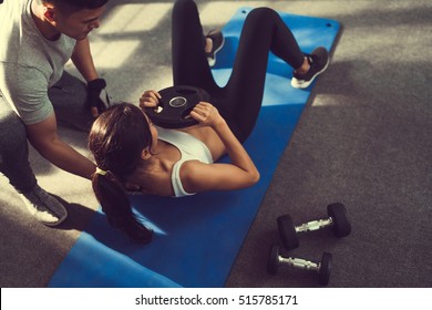 Asian woman are sit-up with added weight on her more and more trainer are there to help. - Powered by Shutterstock