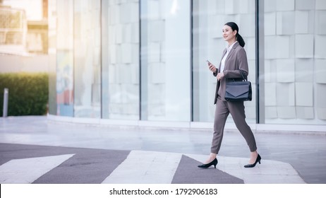 Asian Woman With Smartphone Standing Against Street Blurred Building Background. Fashion Business Photo Of Beautiful Girl In Casual Suite With Smart Phone. 