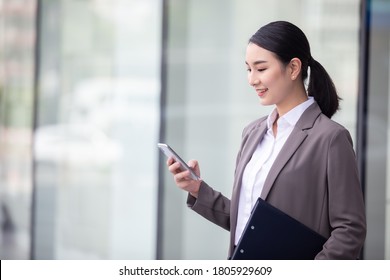 Asian Woman With Smartphone Standing Against Street Blurred Building Background, Fashion Business Photo Of Beautiful Girl In Casual Suite With Smart Phone. 