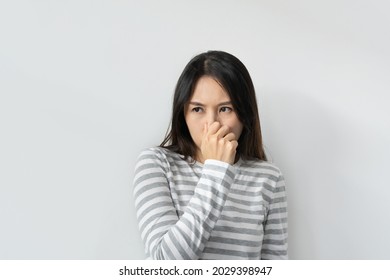 Asian woman smelling something stinky and disgusting, intolerable smell, holding breath with fingers on nose. Girl pinches nose with fingers looks with disgust something stinks bad smell. Copy space