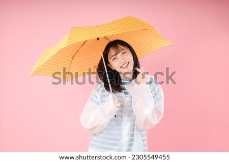 Asian woman smile and make mini heart wearing a rainproof coat and hold an umbrella over pink background