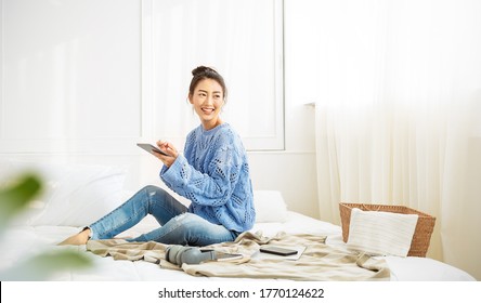 Asian Woman With Smile Use Tablet Smartphone In Blue Winter Sweater Work Home, Portrait Beauty Asia Girl Hygge Relax In Bedroom. Technology People Connection Digital Online Social Media Market Banner