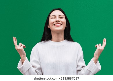 Asian woman smiles broadly with eyes closed, keeps fingers crossed, hope for good luck during exam - Powered by Shutterstock