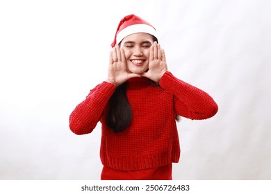 Asian woman smiles broadly keeps palms near rouge face expresses positive emotions wears red turtleneck awaits for holiday event poses against white background - Powered by Shutterstock