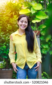 Asian woman smiling happy in park on blurred nature background. Pretty young woman outdoors at daytime with bright sunlight. Beautiful woman tooth smile, a look of enjoyment on face. Positive emotion.