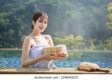 Asian woman is smiling at you holding wooden bucket in the hotspring