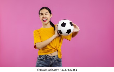 Asian Woman Smilling In Yellow T-shirt Holding Football Ball To Cheering The Soccer Game On The Pink Screen Background.