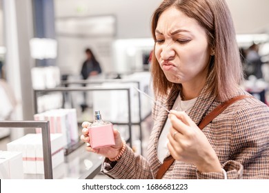 Asian Woman Sniffs Perfume With A Disgusting And Terrible Fragrance. Concept Of Bad Taste And Loss Of Smell