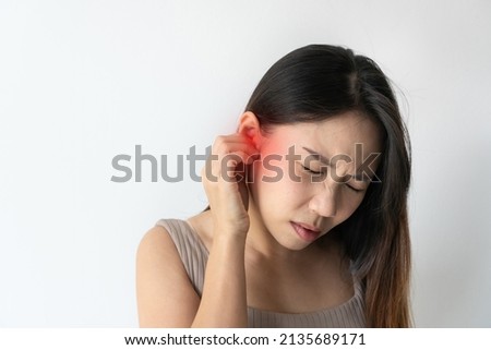 Asian woman with sore ear suffering from otitis with red accent. Stressed frowning young girl from strong ear pain feeling painful discomfort isolated on white studio background. Copy space, closeup