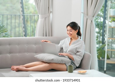 A Asian Woman Spending Time At Home, Sitting On Sofa, Using Her Laptop