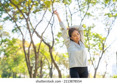 Asian woman in sportswear and smartwatch stretching body while jogging at public park in the city in the morning. Healthy female athlete enjoy outdoor lifestyle sport training workout running exercise