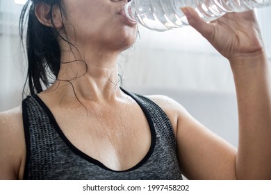 Asian Woman In Sportwear Drinking Fresh Water From Bottle  After Doing Sport , Sweating And Tired From Exercise 