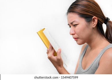 Asian Woman Squinting With Poor Eyesight Have Difficulty Reading Book On White Background, Selective Focus On Glasses , Myopia And Eyesight Problem Concept.