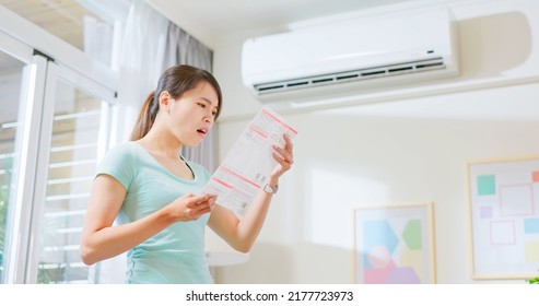 asian woman stand by air conditioner shocked and upset about electricity bill in hand at home - economic inflation concept - Shutterstock ID 2177723973