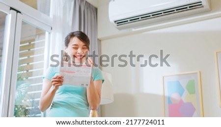 asian woman stand by air conditioner smile happily posing fist gesture about electricity bill saving in hand at home - economic inflation concept
