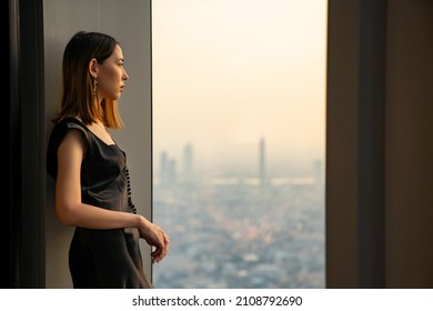 Asian woman standing by the window at skyscraper office building in metropolis and looking cityscape at summer sunset. Beautiful female relax and enjoy outdoor lifestyle activity in the city at night - Powered by Shutterstock