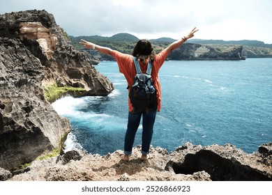 Asian woman standing with her back and raise her arms for freedom life on the rocky cliff of calm sea. Destination backpack travel on summer with ocean in Bali island at Indonesia - Powered by Shutterstock