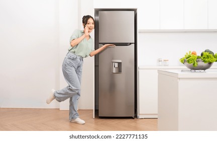 Asian woman standing next to the refrigerator in the kitchen - Shutterstock ID 2227771135