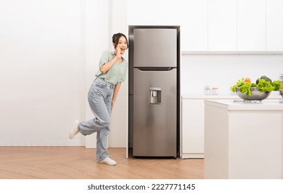 Asian woman standing next to the refrigerator in the kitchen - Shutterstock ID 2227771145