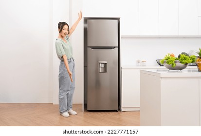 Mujer asiática parada al lado del refrigerador en la cocina