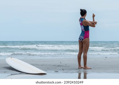 Asian woman standing on the beach, she is warming up by stretching her arms. before surfing in the sea. to people recreation and exercise by surf concept. - Powered by Shutterstock