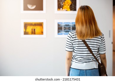 Asian Woman Standing She Looking Art Gallery In Front Of Colorful Framed Paintings Pictures On White Wall, Young Female Watch At Photo Frame To Leaning Against At Show Exhibition Gallery, Back View
