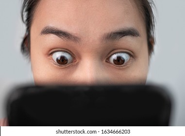 Asian woman staring at her smartphone screen all day. Focused on eyes. Mobile phone addiction. - Shutterstock ID 1634666203