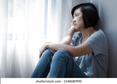 An Asian woman is staring outside the window. She has symptoms of depression, stress and gloom.