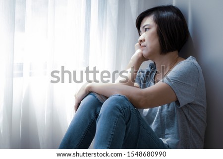 An Asian woman is staring outside the window. She has symptoms of depression, stress and gloom.