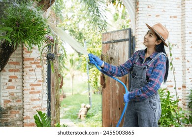 Asian woman, straw hat, blue gloves, waters hanging plant, stream of water in focus. garden gate partially visible. sitting in a green garden. flower garden owner Taking care of trees for sale - Powered by Shutterstock