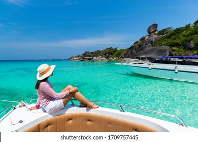 Asian woman with straw hat travel at Thailand sea.Tourist is sitting and relaxing on speed boat near white sandy beach,In vacation or summer time,Similan Iceland is very warm and perfect for leisure.