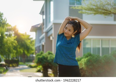 Asian woman stretching to warm up or cool down, before or after exercise, near the front door in the neighborhood for daily health and well being, both physical and mental.