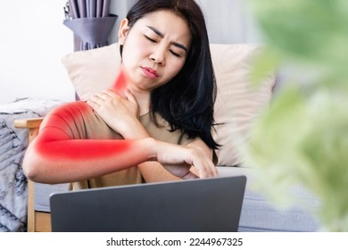 Asian woman suffering from neck pain spreading to shoulder and down arm caused by overworked on a computer with bad posture 
