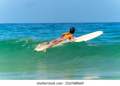 Asian Woman Surfer Paddling Surfboard And Riding The Wave In The Sea At Tropical Beach In Sunny Day. Healthy Female Enjoy Outdoor Activity Lifestyle And Water Sport Exercise Surfing On Summer Vacation