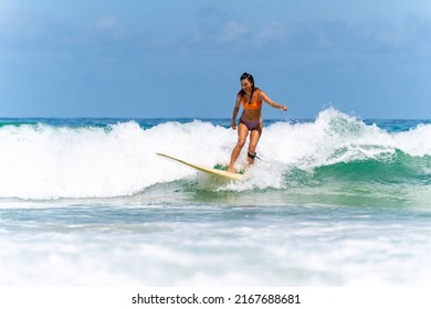 Asian Woman Surfer Surfing And Riding Surfboard  The Wave In The Sea At Tropical Beach In Sunny Day. Healthy Female Enjoy Outdoor Activity Lifestyle And Water Sport Exercise Surfing On Summer Vacation