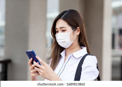 Asian woman with surgical mask face protection - she use a smartphone while walking outside in the city - Powered by Shutterstock