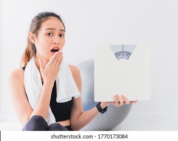 Asian woman are surprised and holding weighing scale after play yoga and exercise at home.Expressing worry about body weight, weight loss.