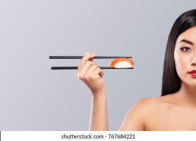 Asian woman with sushi eating sushi and rolls on a gray background. Copy space.
