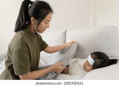 asian woman take care of little ill daughter. Sick child lying on bed under blanket, with worried. single mom taking care of sick daughter at home. child has a high fever. covers on the couch and ill - Powered by Shutterstock