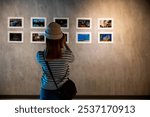 Asian woman takes picture art gallery collection in front framed paintings pictures on white wall with camera, Photographer watch at photo frame to leaning against at show exhibit artwork gallery