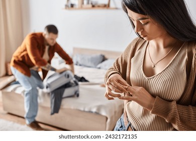 asian woman taking off wedding ring while husband packing suitcase in bedroom, family divorce - Powered by Shutterstock