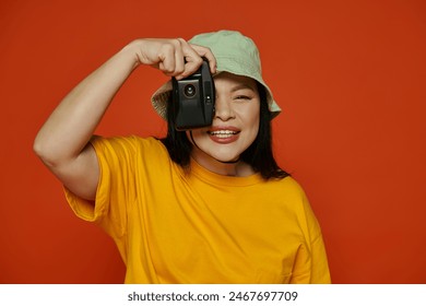 An Asian woman taking a picture, using a retro camera on an orange background. - Powered by Shutterstock