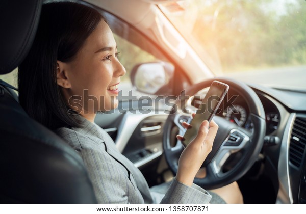 Asian woman talk by mobile calling texting and\
looking on a cellular phone while sitting in her car, driving under\
the influence, the driver is safely talking by smartphone in a car\
concept