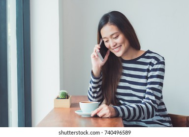 Asian Woman Talking On Mobile Phone And Sitting At Cafe Restaurant Near Window See Through Garden,Digital Age Lifestyle,Working Outside Office Concept.