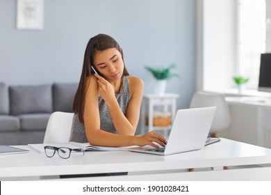 Asian woman talking on phone using office laptop computer. Personal business assistant or magazine editor browsing web, booking tickets online, entering order into database or planning boss's schedule