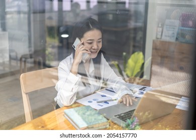 Asian Woman Talking On The Phone, She Is A Salesperson In A Startup Company, She Is Calling Customers To Sell Products And Promotions. Concept Of Selling Products Through Telephone Channels.