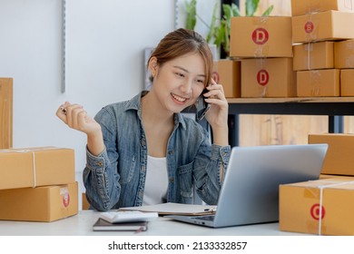 Asian Woman Is Talking On The Phone With A Customer To Confirm An Order, She Owns An Online Store, She Packs And Ships Through A Private Transport Company. Online Selling And Online Shopping Concepts.