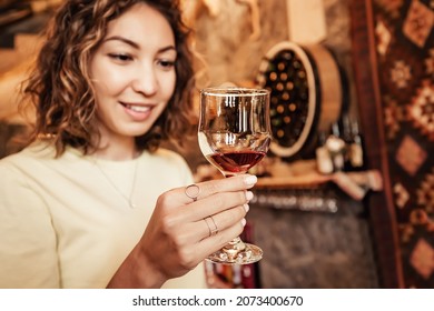 An Asian Woman Tastes And Analyzes Wine In The Cellar Of A Local Winery. Concept Of Tours And Sommelier Work