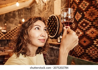 An Asian Woman Tastes And Analyzes Wine In The Cellar Of A Local Winery. Concept Of Tours And Sommelier Work